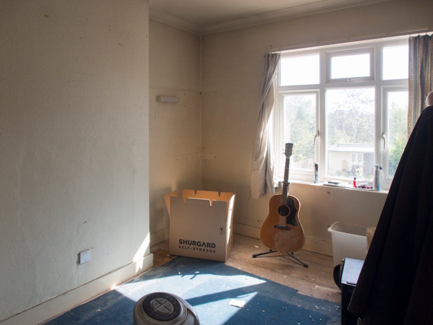 A professional cleaner from Wimbledon Cleaner is performing deep surface cleaning on a large glass window using a mop and a squeegee, wearing protective white coveralls, gloves, and a face mask. The i